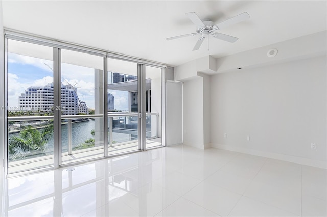 tiled spare room featuring expansive windows, a water view, a ceiling fan, baseboards, and a view of city