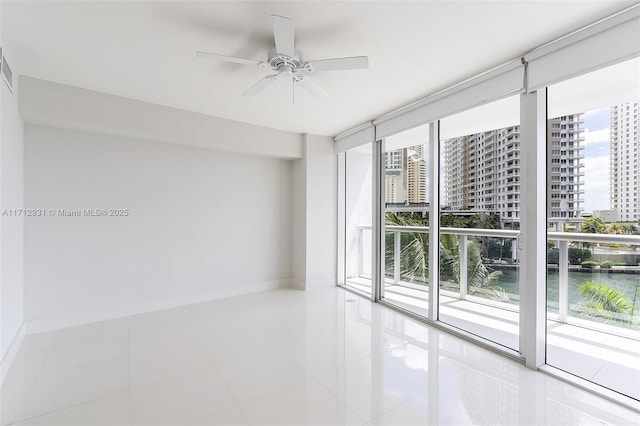 unfurnished room with a ceiling fan, baseboards, floor to ceiling windows, tile patterned floors, and a view of city