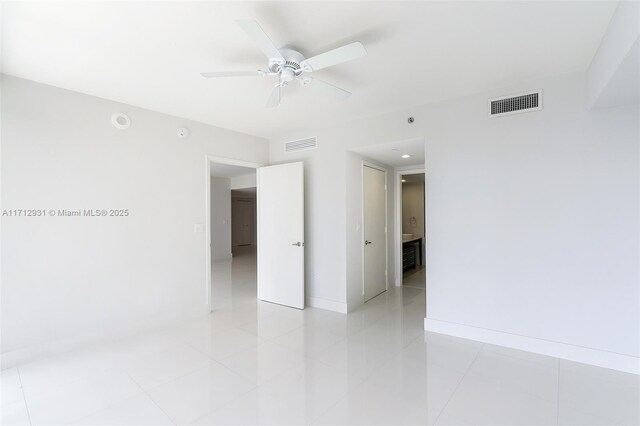 empty room with light tile patterned floors, a ceiling fan, visible vents, and baseboards