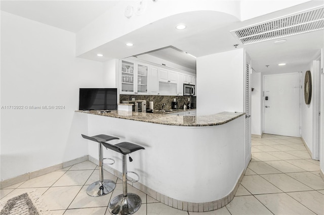 kitchen with kitchen peninsula, decorative backsplash, light tile patterned floors, stone counters, and white cabinetry