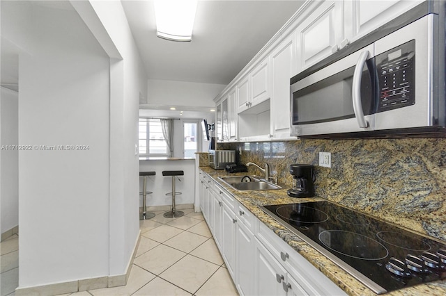 kitchen featuring black electric stovetop, tasteful backsplash, dark stone counters, sink, and white cabinets