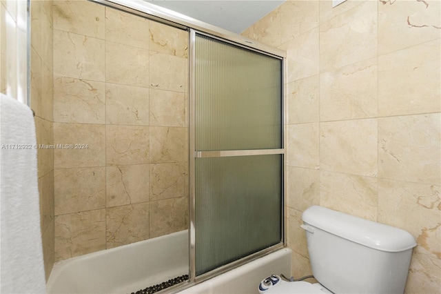 bathroom with combined bath / shower with glass door, tile walls, and toilet