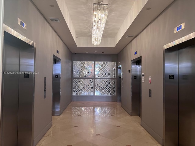 hall with a tray ceiling, elevator, and an inviting chandelier