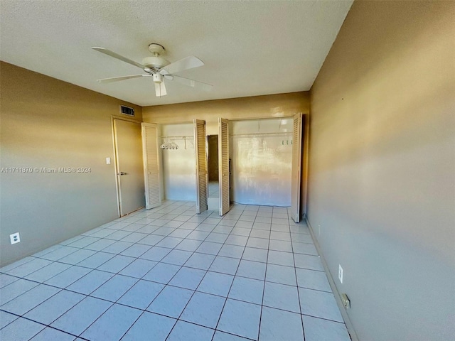 unfurnished bedroom with a textured ceiling, ceiling fan, light tile patterned flooring, and two closets