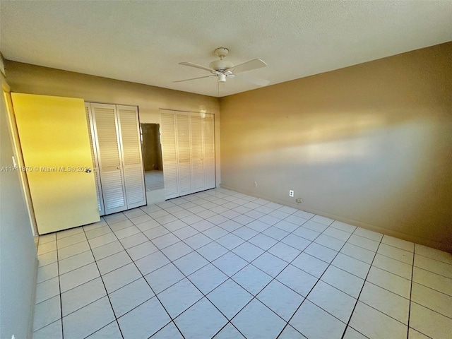 unfurnished bedroom with ceiling fan, light tile patterned floors, a textured ceiling, and two closets