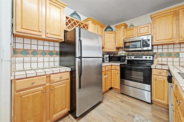 kitchen featuring backsplash, appliances with stainless steel finishes, light hardwood / wood-style flooring, and tile countertops