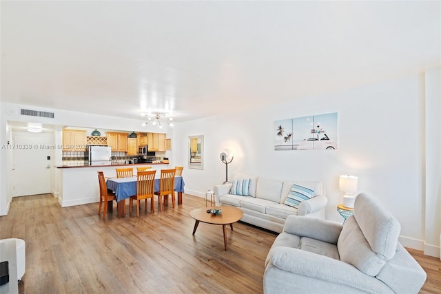 living area featuring light wood-style flooring, visible vents, and baseboards