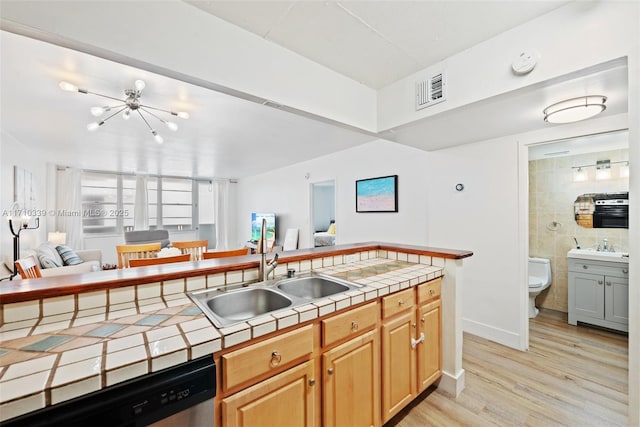 kitchen featuring tile counters, open floor plan, stainless steel dishwasher, light wood-style floors, and a sink