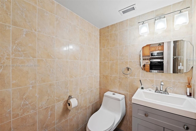 bathroom featuring visible vents, decorative backsplash, toilet, vanity, and tile walls