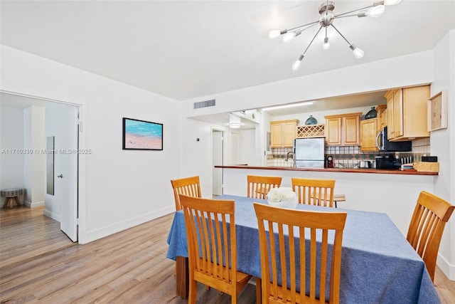 dining area with light wood-type flooring, visible vents, and baseboards