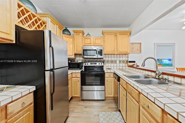 kitchen featuring tile countertops, stainless steel appliances, a sink, light brown cabinetry, and tasteful backsplash