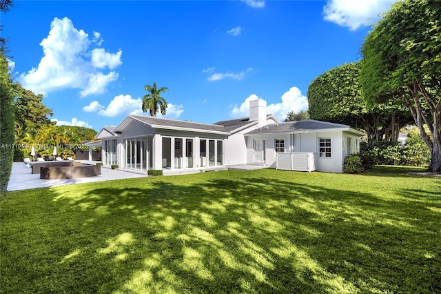back of property featuring a patio, stucco siding, a chimney, a sunroom, and a lawn