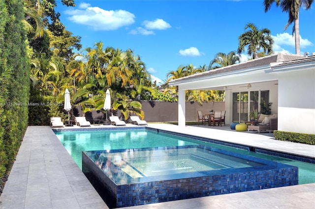 outdoor pool with a patio, fence, and an in ground hot tub