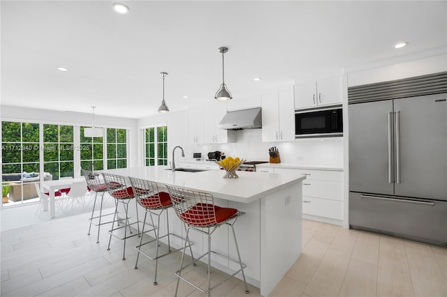 kitchen with pendant lighting, built in appliances, extractor fan, and an island with sink