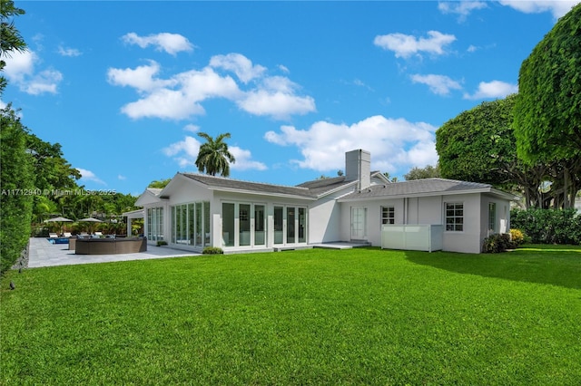 back of property with a patio, a chimney, stucco siding, and a lawn