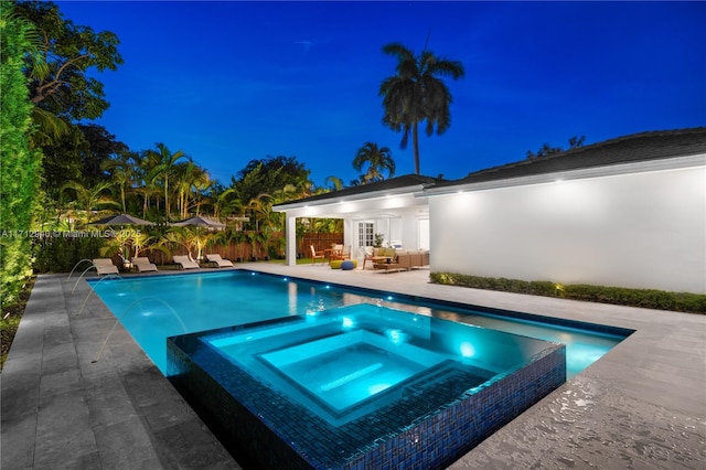 pool at night featuring a patio, a pool with connected hot tub, and a fenced backyard