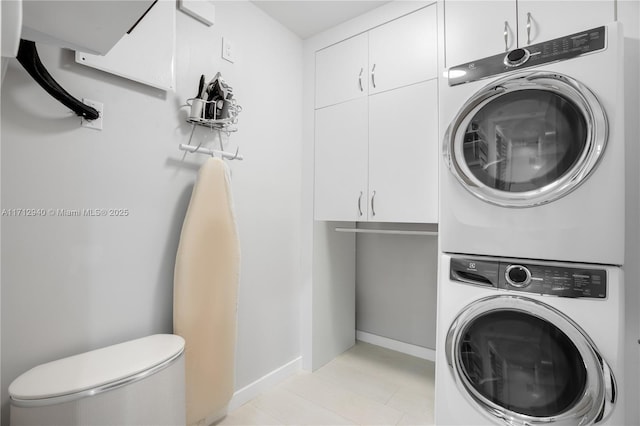 washroom with stacked washer and dryer, baseboards, and cabinet space