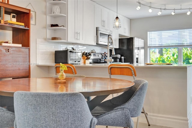 kitchen featuring backsplash, a kitchen breakfast bar, hanging light fixtures, white cabinetry, and stainless steel appliances