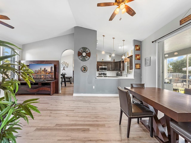 dining room featuring ceiling fan, arched walkways, light wood-type flooring, and lofted ceiling