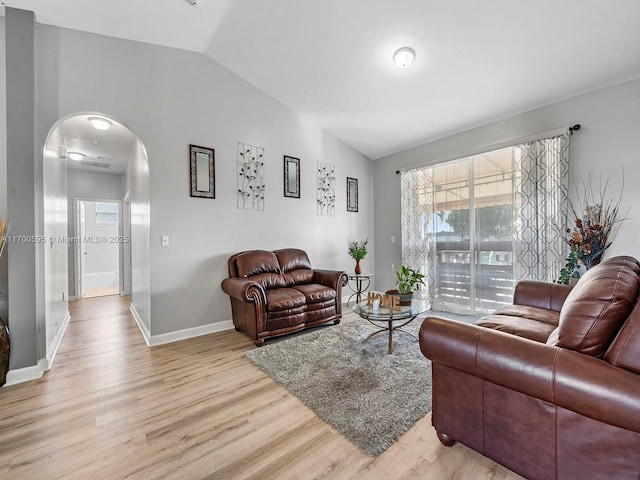 living area featuring arched walkways, light wood finished floors, lofted ceiling, and baseboards