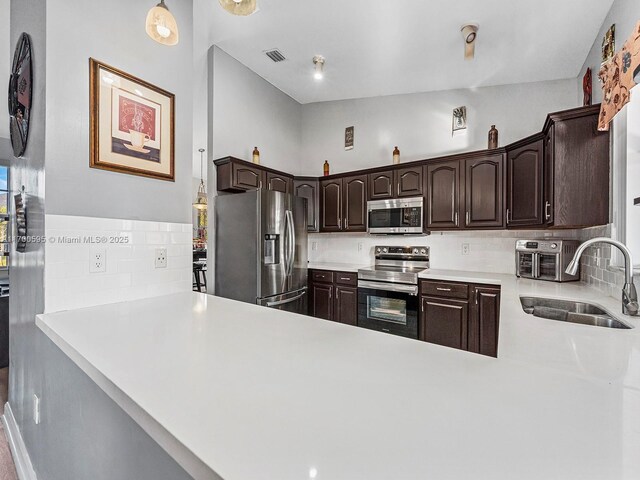 kitchen featuring appliances with stainless steel finishes, kitchen peninsula, dark brown cabinetry, and sink