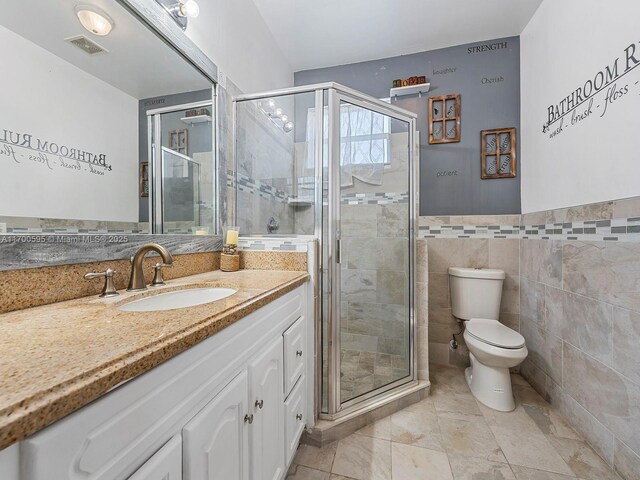 bathroom featuring toilet, vanity, tile walls, and a shower with door