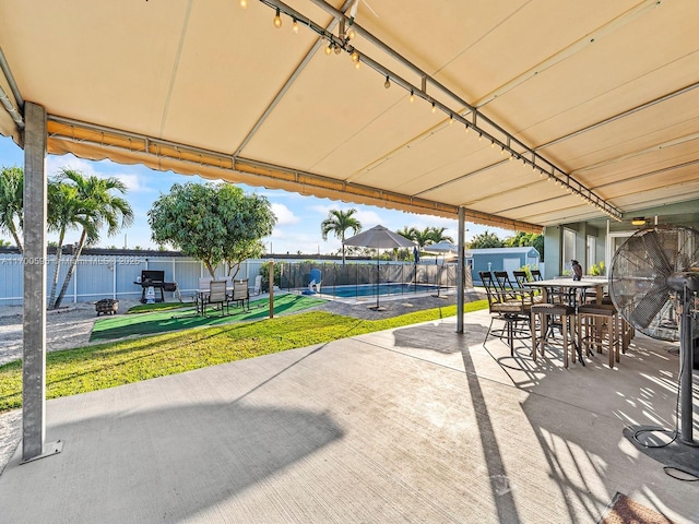 view of patio / terrace with an outbuilding, outdoor dining space, fence, and a fenced in pool