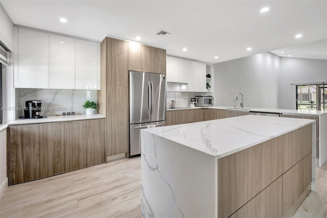 kitchen featuring sink, stainless steel fridge, light stone countertops, light hardwood / wood-style floors, and white cabinetry