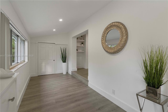 hallway featuring wood-type flooring, built in features, and lofted ceiling