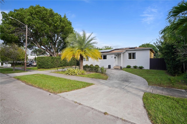 single story home featuring solar panels and a front lawn