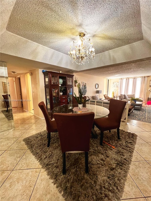 tiled dining space with a notable chandelier, a textured ceiling, and a tray ceiling