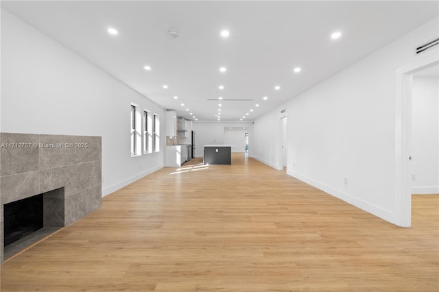 unfurnished living room with light wood-style flooring, recessed lighting, baseboards, and a tile fireplace