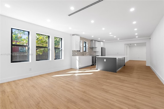 kitchen featuring light wood finished floors, a kitchen island, wall chimney exhaust hood, white cabinets, and light countertops