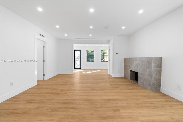 unfurnished living room with recessed lighting, a tile fireplace, light wood-type flooring, and baseboards