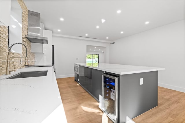 kitchen with a spacious island, a sink, decorative backsplash, wine cooler, and wall chimney exhaust hood