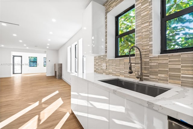 kitchen featuring light stone countertops, light wood-type flooring, a sink, white cabinets, and tasteful backsplash