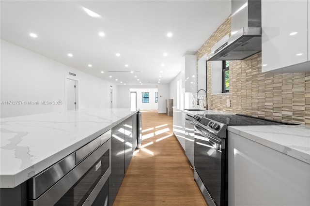 kitchen with backsplash, stainless steel electric stove, light wood-style floors, modern cabinets, and wall chimney exhaust hood