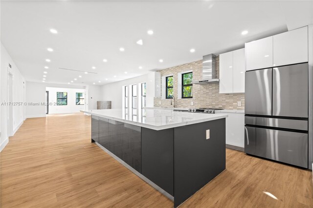 kitchen with wall chimney range hood, a spacious island, white cabinets, and stainless steel refrigerator