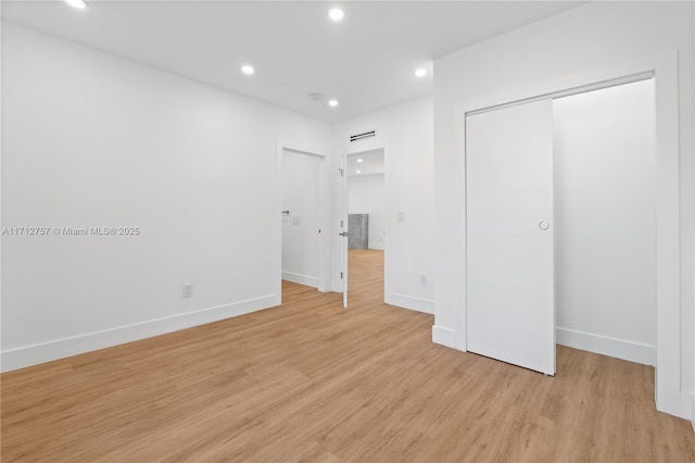 unfurnished bedroom with baseboards, light wood-style flooring, recessed lighting, a closet, and a barn door