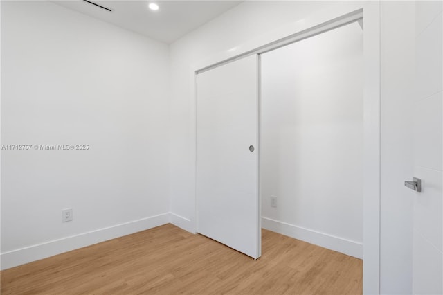 unfurnished bedroom featuring light wood finished floors, baseboards, and a closet