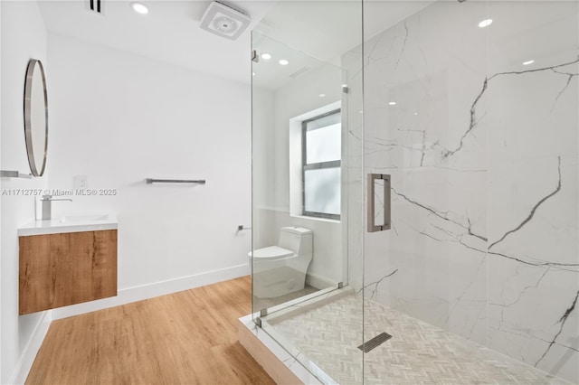 bathroom featuring vanity, wood finished floors, baseboards, and a marble finish shower