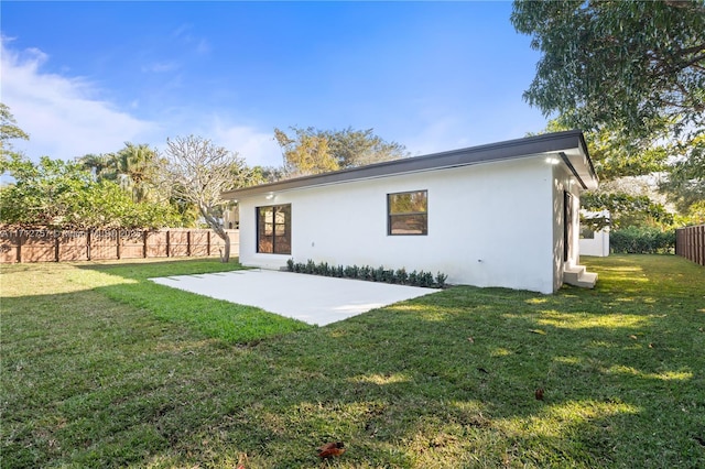 back of property with stucco siding, a lawn, a patio, and fence