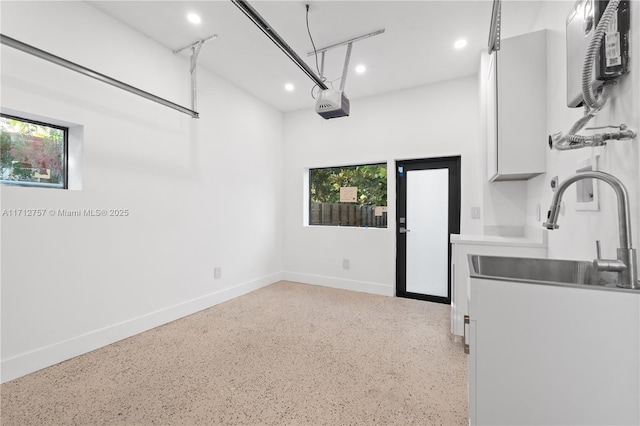 garage with recessed lighting, a garage door opener, baseboards, and a sink