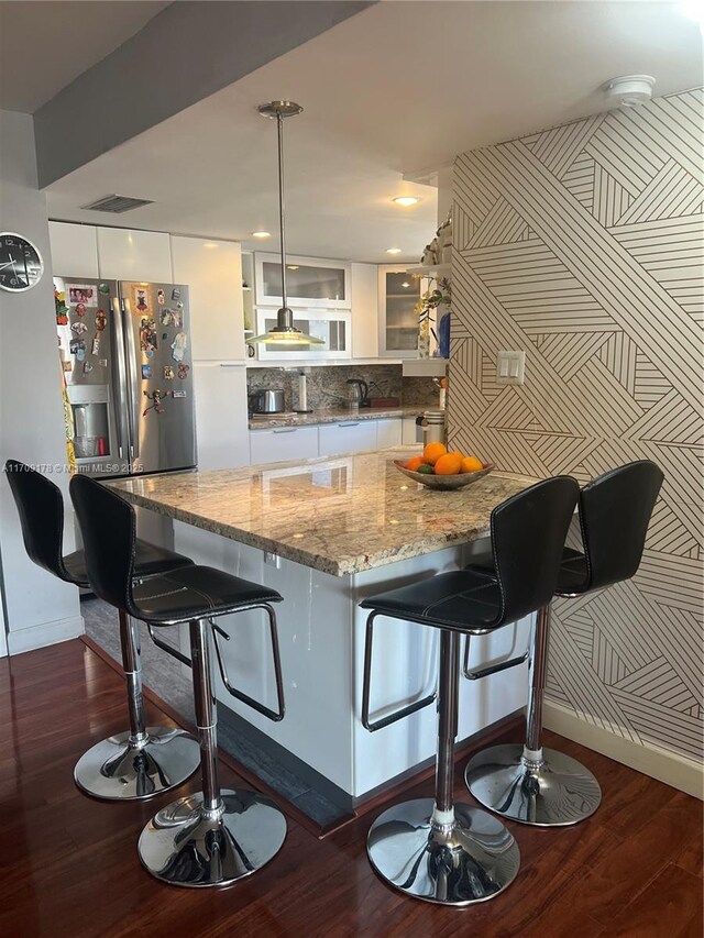 kitchen featuring dark hardwood / wood-style flooring, stainless steel fridge, decorative light fixtures, a breakfast bar, and white cabinets