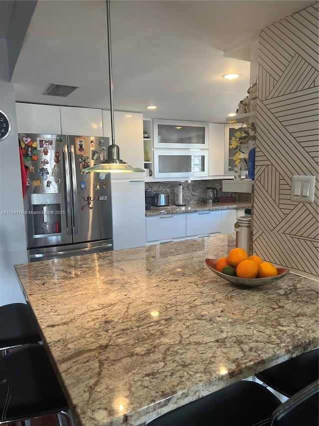 kitchen featuring white cabinetry, stainless steel fridge with ice dispenser, hanging light fixtures, and a kitchen bar