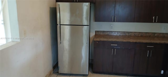 kitchen with dark brown cabinetry, stainless steel fridge, and light tile patterned floors