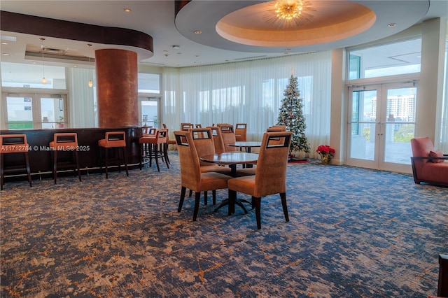 dining area featuring french doors, dark carpet, and a raised ceiling