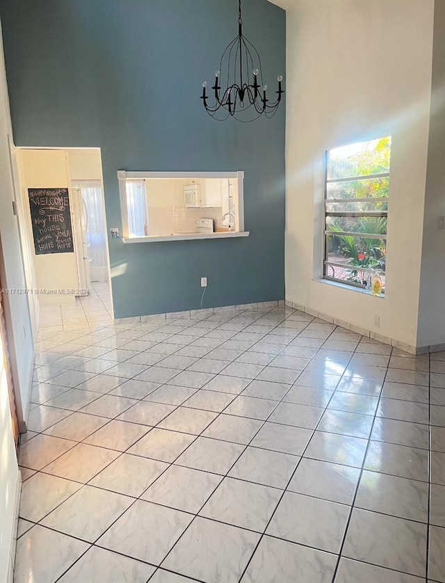 tiled empty room featuring a chandelier and a high ceiling