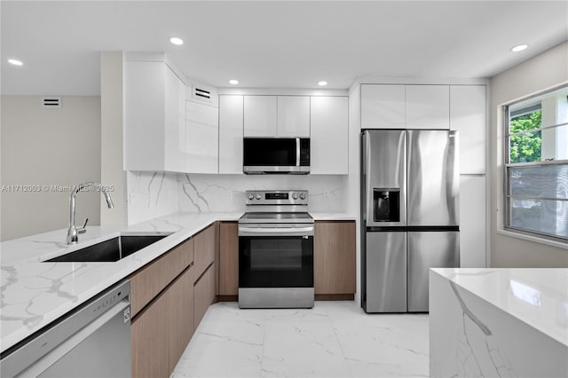 kitchen featuring white cabinetry, sink, stainless steel appliances, light stone counters, and decorative backsplash