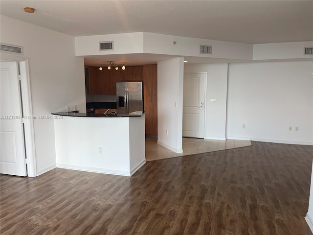 kitchen featuring kitchen peninsula, stainless steel refrigerator with ice dispenser, dark brown cabinetry, and hardwood / wood-style flooring